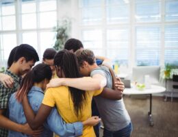 Group of happy business executives forming huddle in office