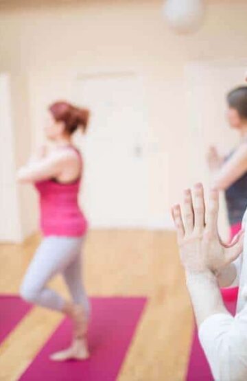 Group of people performing tree-pose yoga exercise in the fitness studio